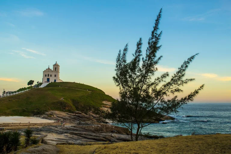 Igreja de Nossa Senhora de Nazareth no alto do morro, com pedras e o mar ao entardecer, em Saquarema