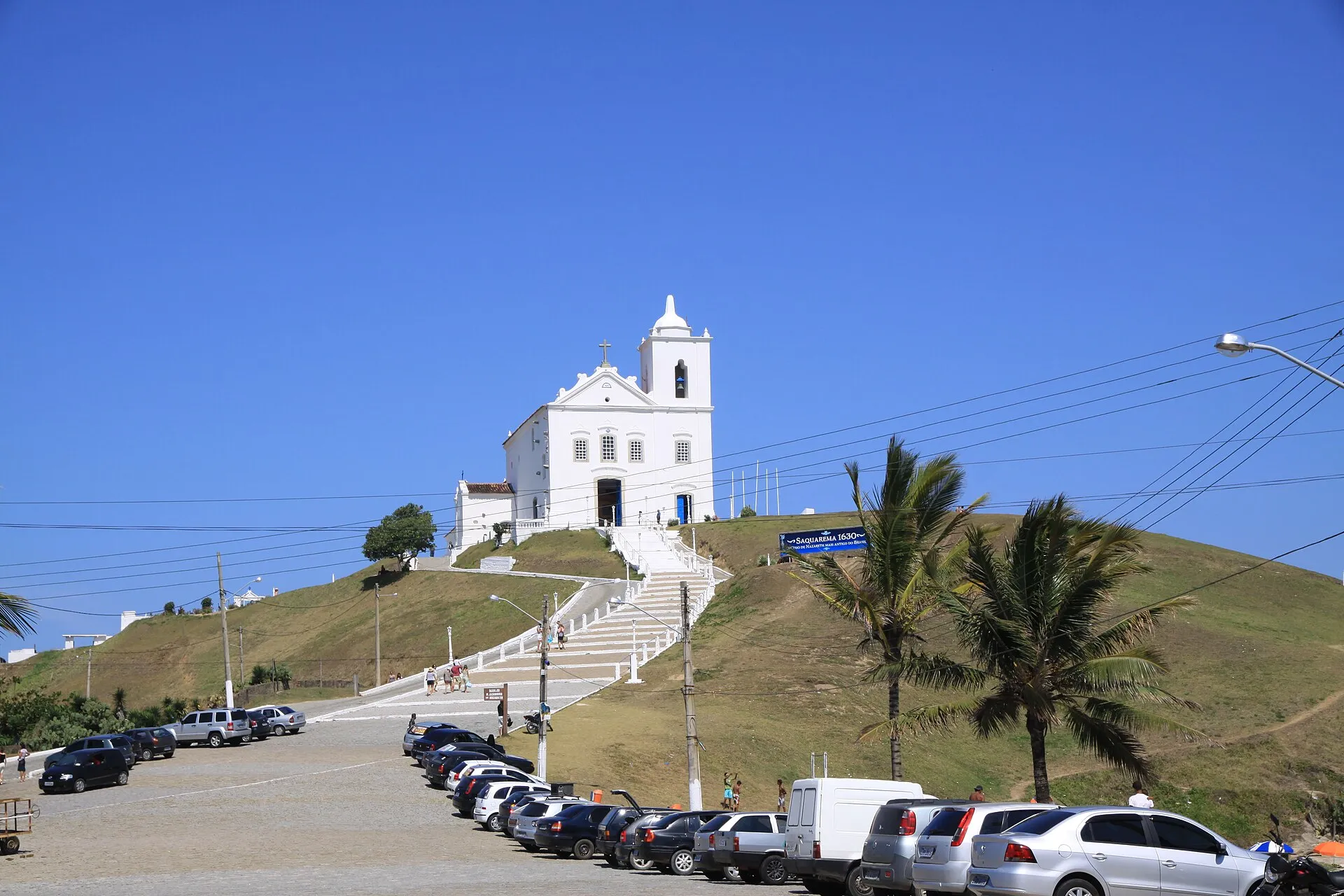 Igreja branca de Nossa Senhora de Nazaré no alto do morro do centro histórico de Saquarema, com escadaria e estacionamento ao pé