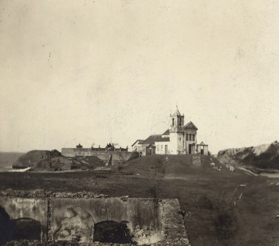 Fotografia antiga em sépia da Igreja de São João no alto do morro de Barra de São João, com muros de pedra em primeiro plano