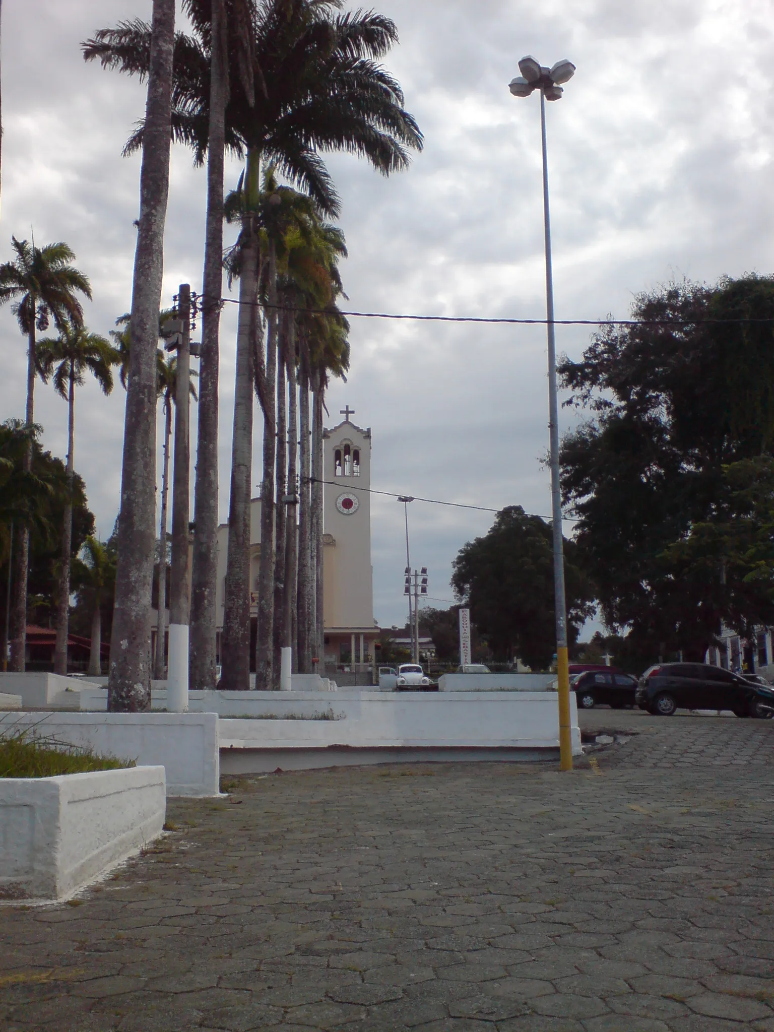 Torre branca da Igreja de São Sebastião ao fundo de uma praça com palmeiras-imperiais, no centro de Araruama