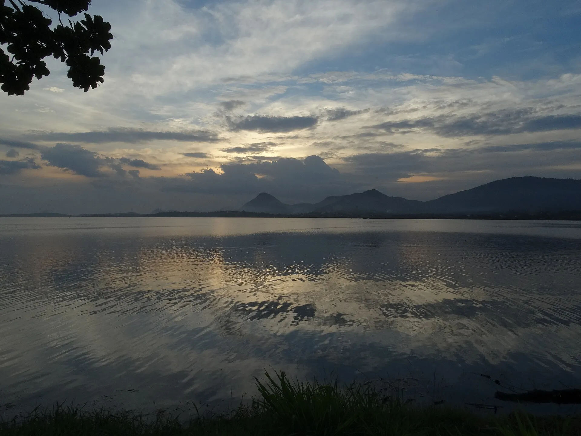 Lagoa de Araçatiba ao entardecer, com águas calmas refletindo o céu nublado e montanhas ao fundo