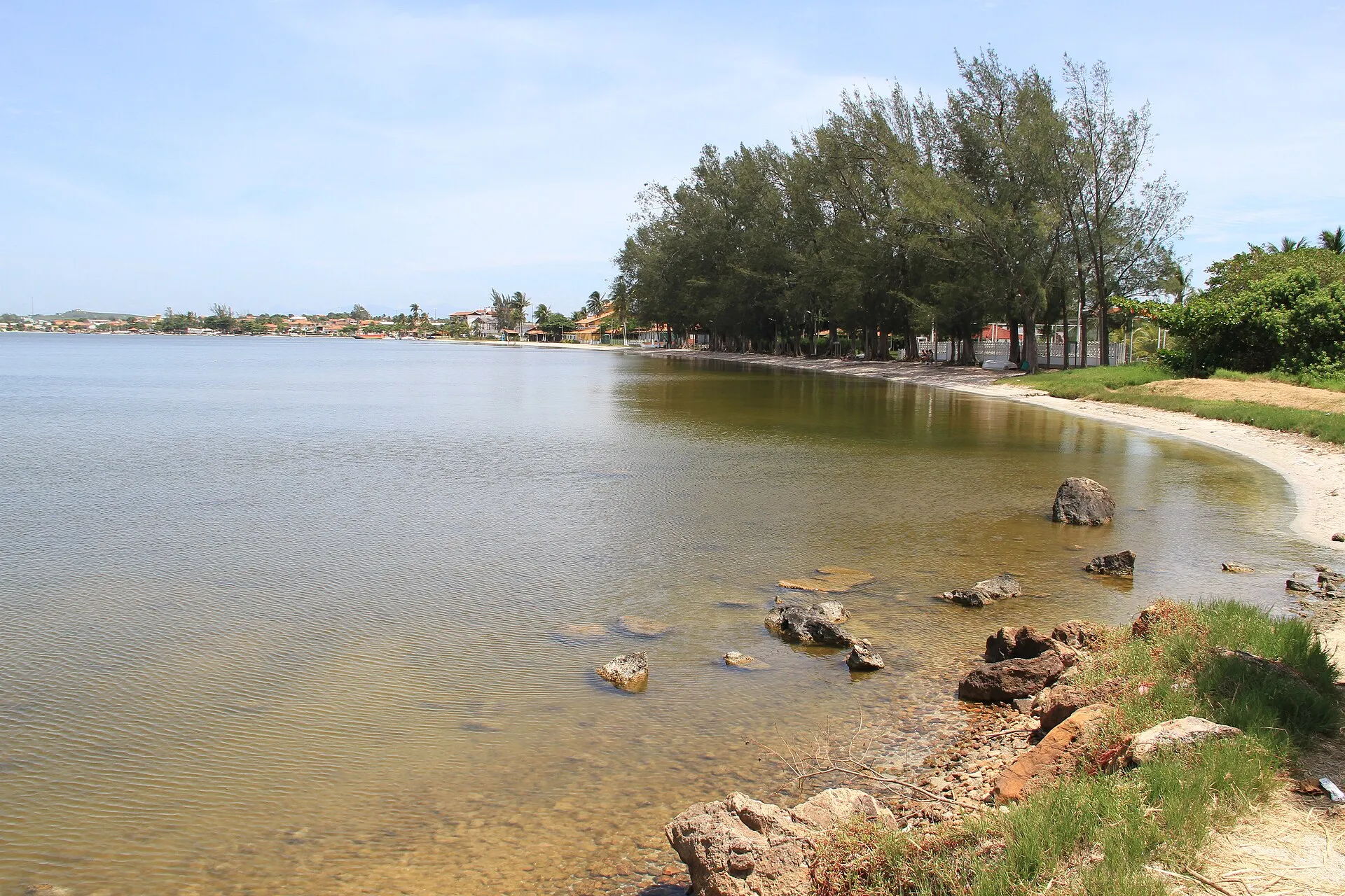 Margem da Lagoa de Araruama em Iguaba Grande, com águas rasas e transparentes, pedras e árvores na orla