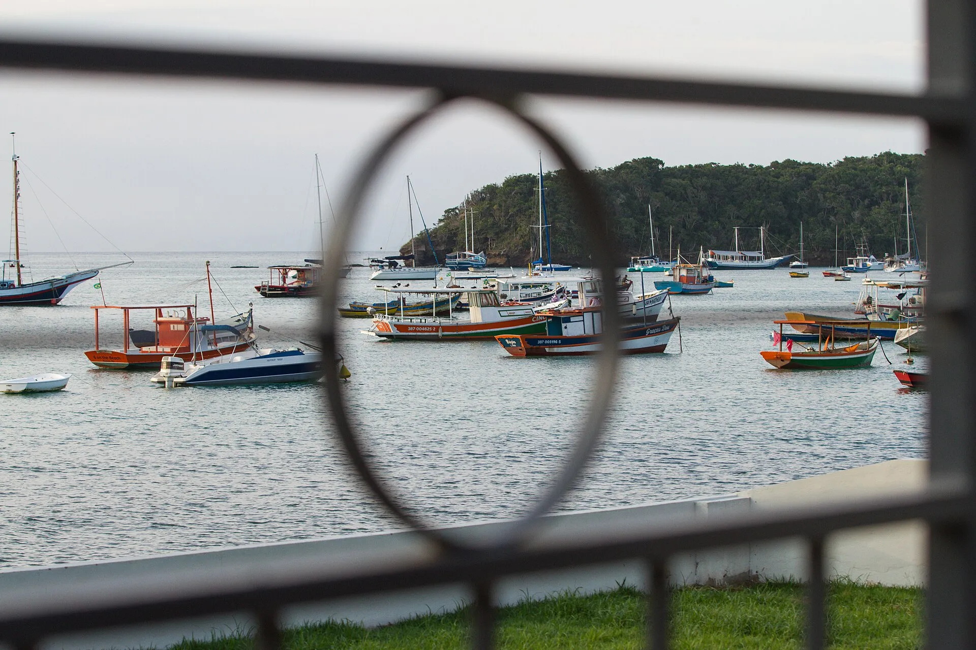 Barcos coloridos ancorados na enseada de Búzios, vistos através do guarda-corpo da Orla Bardot