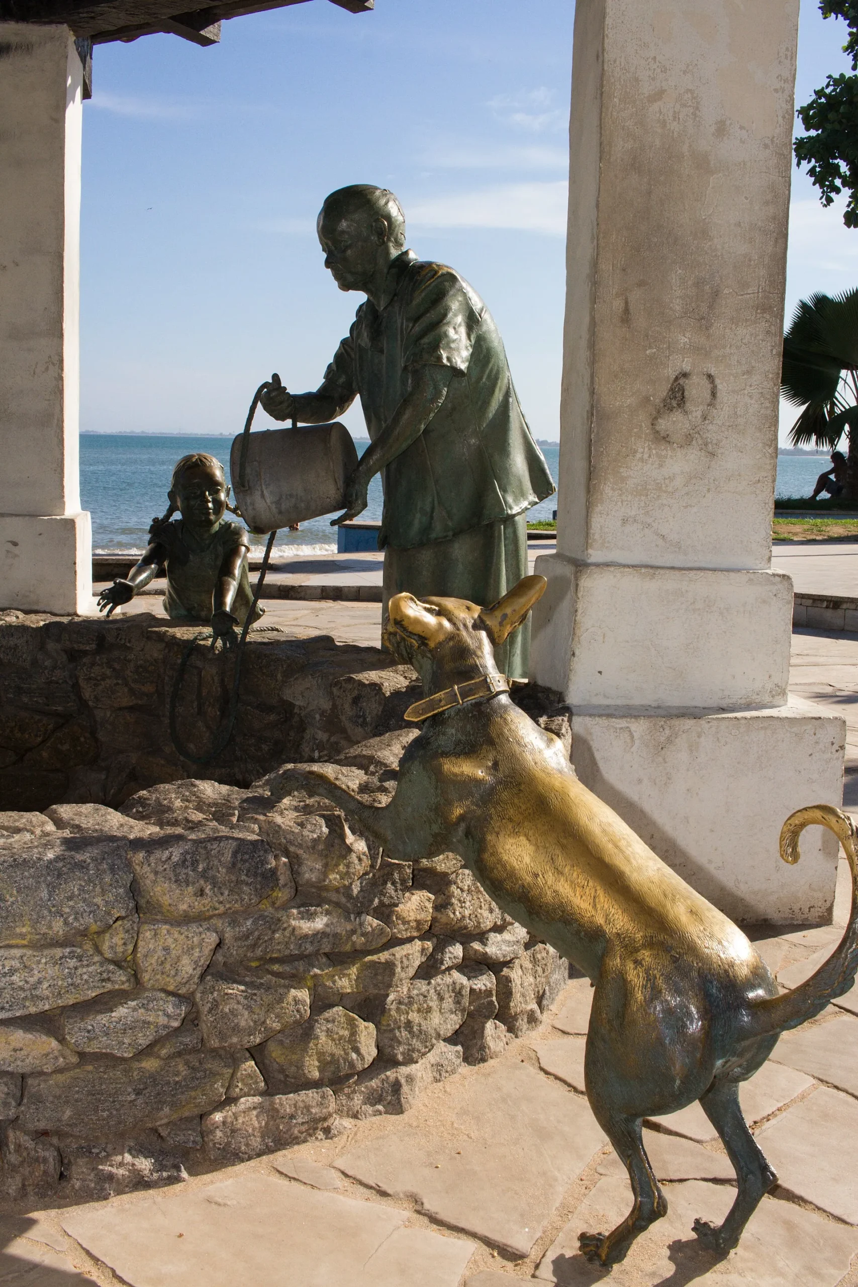 Esculturas de bronze de uma moradora tirando água, uma menina e um cachorro junto ao antigo Poço de Pedras, à beira-mar em Rio das Ostras