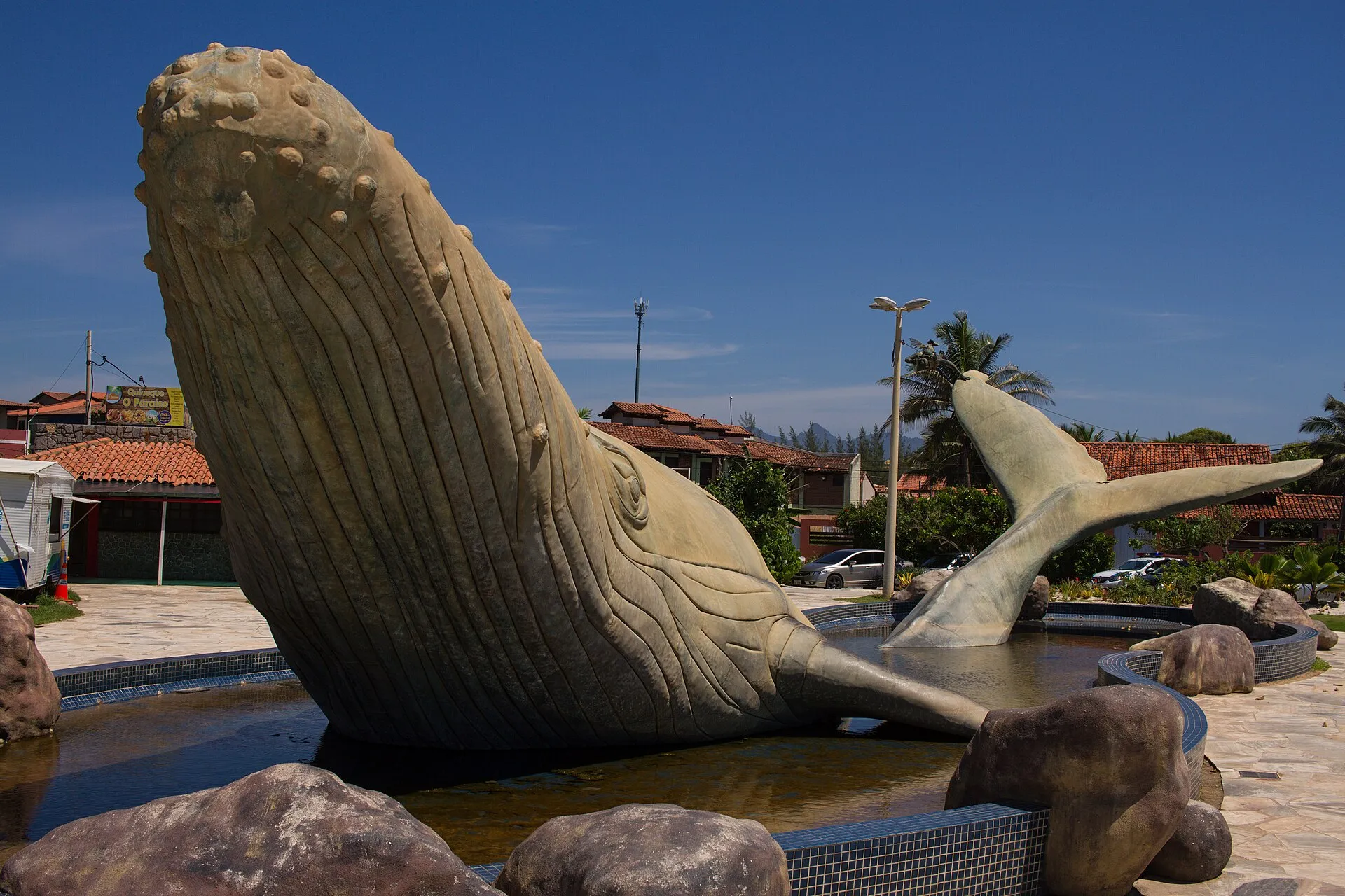 Grande escultura de baleia-jubarte saltando sobre pedras, com a cauda erguida, na Praça da Baleia, em Rio das Ostras