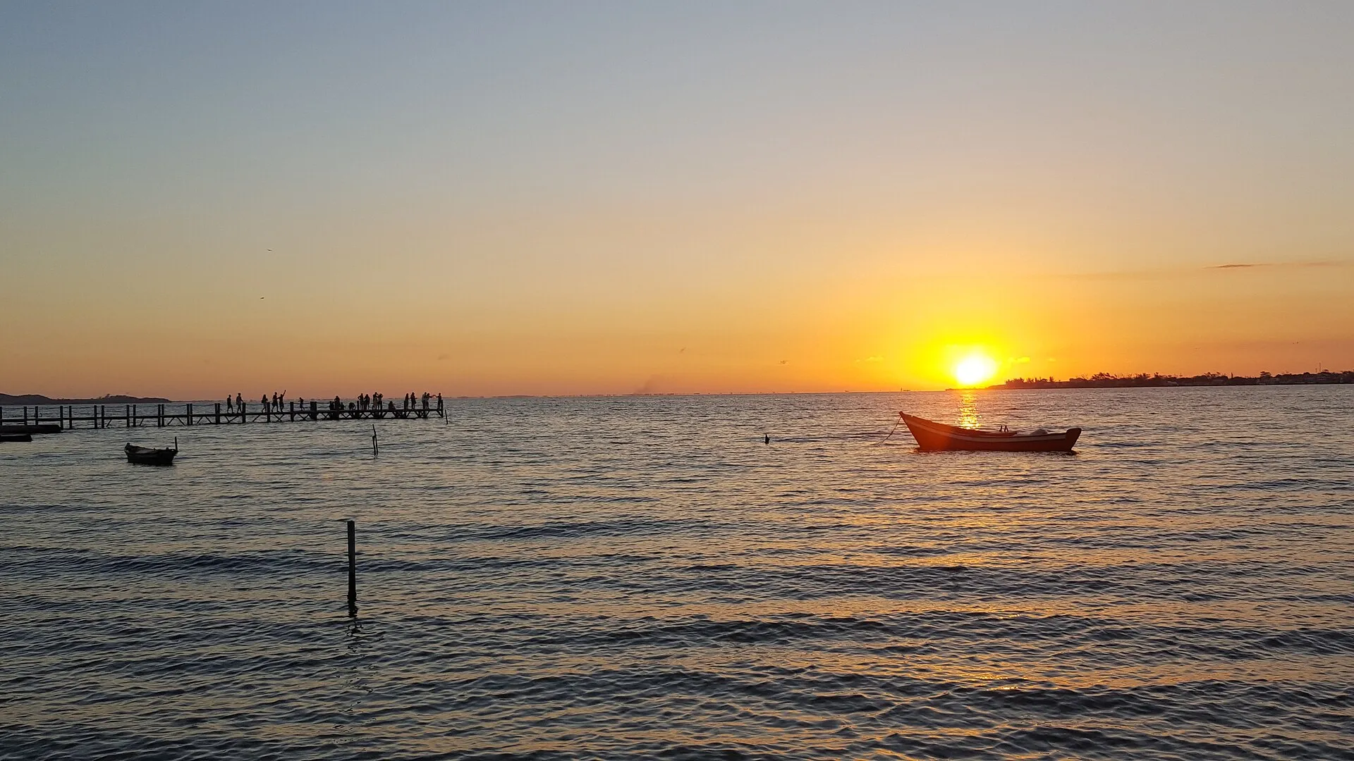 Pôr do sol sobre a Lagoa de Araruama na praia do centro de São Pedro da Aldeia, com barcos e um píer de madeira