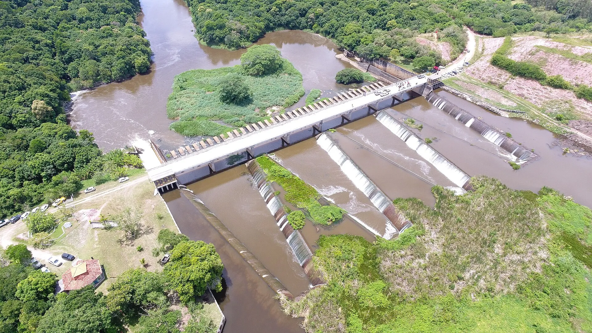 Vista aérea do vertedouro da Represa de Juturnaíba, com a barragem de concreto atravessando o rio entre áreas verdes