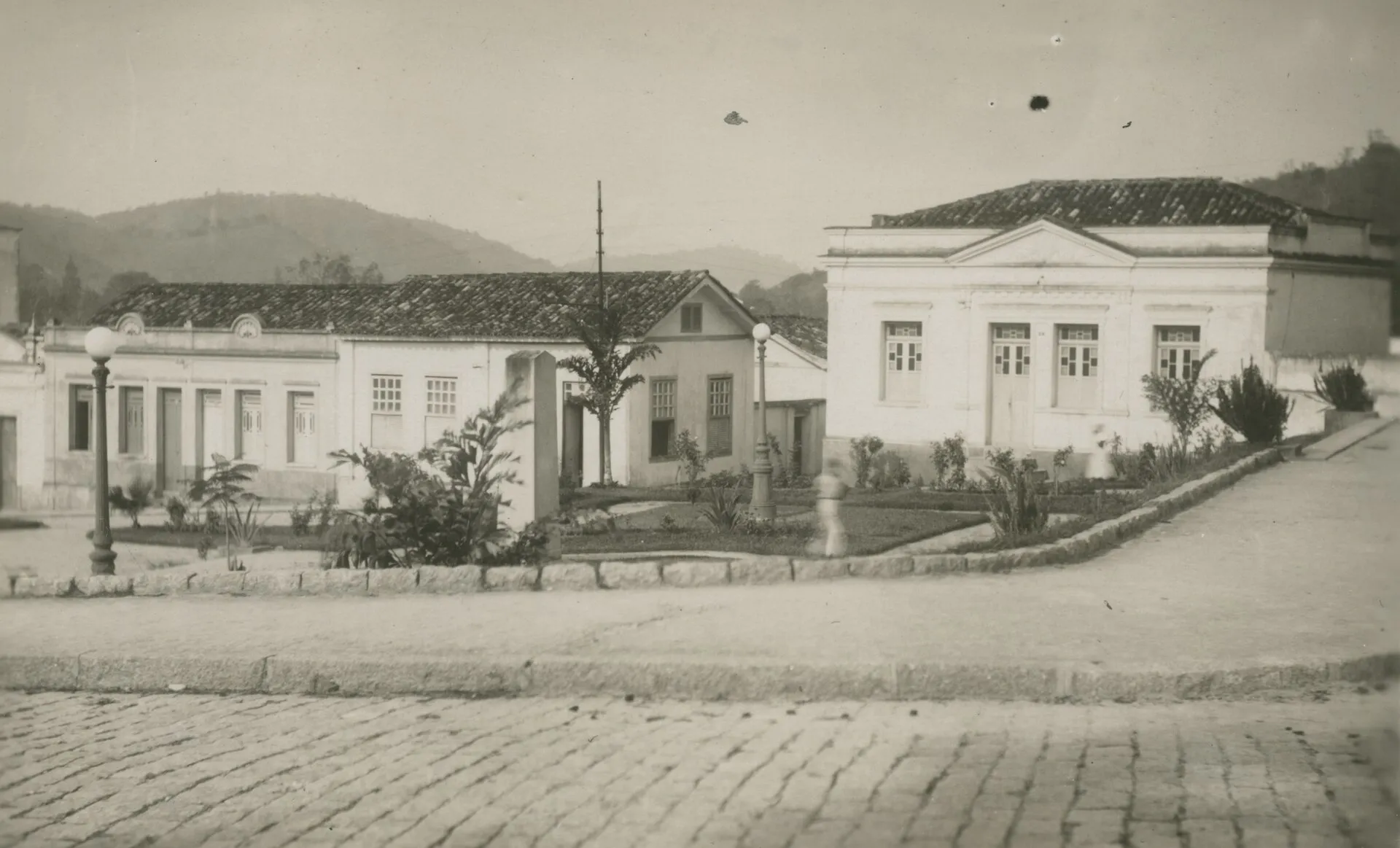 Fotografia antiga em sépia de uma praça de Rio Bonito em 1945, com casarões térreos e calçamento de pedras