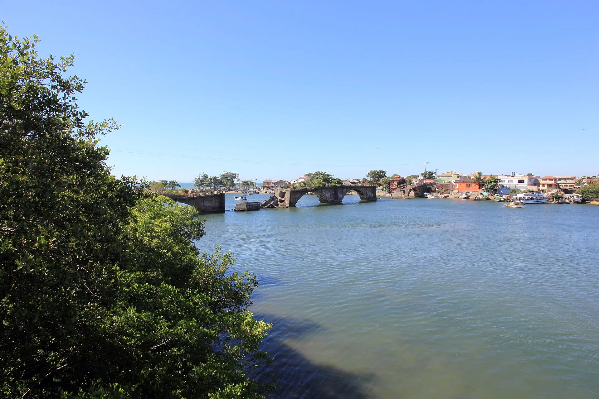 Rio São João em Barra de São João, com a ponte e casas na margem oposta, emoldurado por árvores