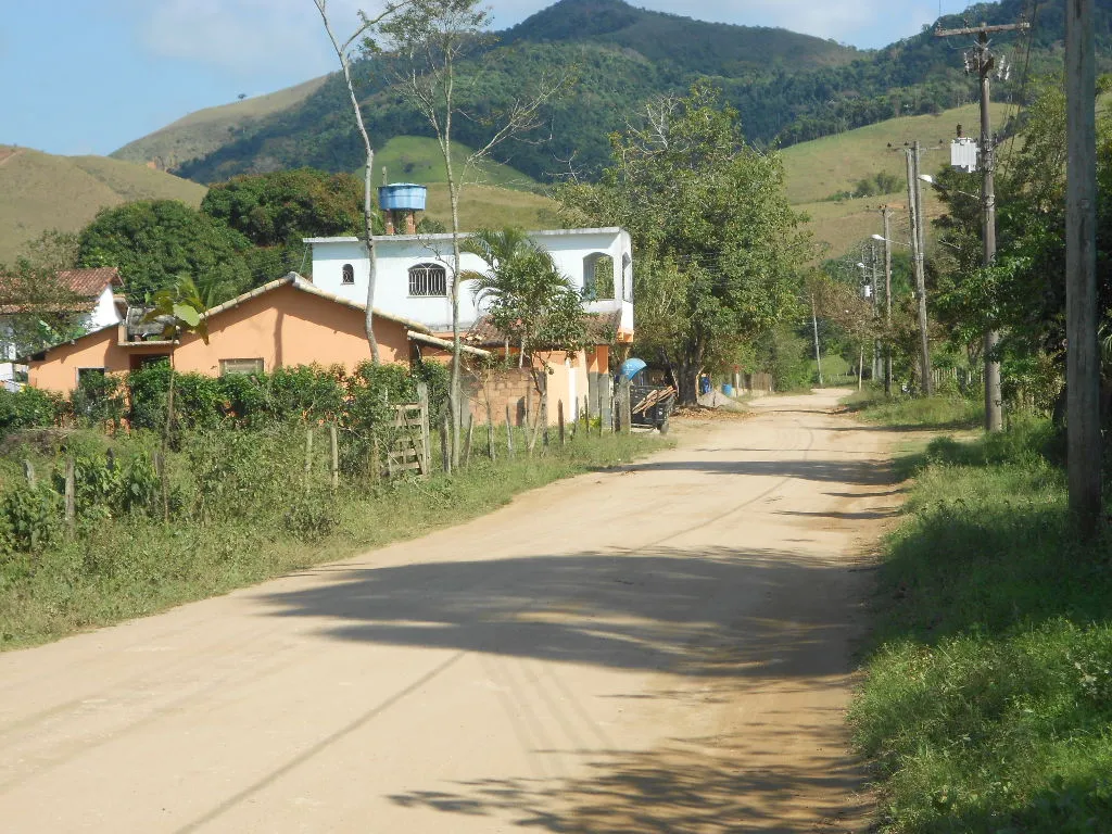 Estrada de terra na zona rural de Silva Jardim, com casas simples e morros verdes ao fundo